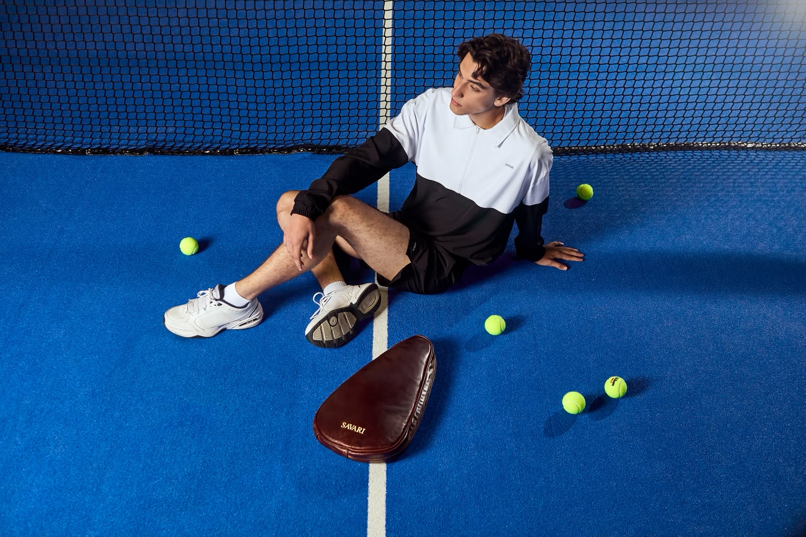 Padel player seated on a blue court beside a brown Savari leather bag