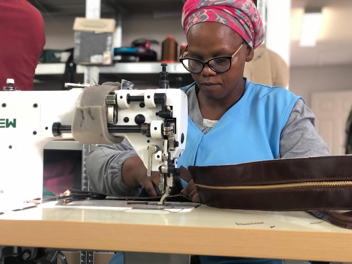 A craftsperson working on a brown leather bag at a sewing machine